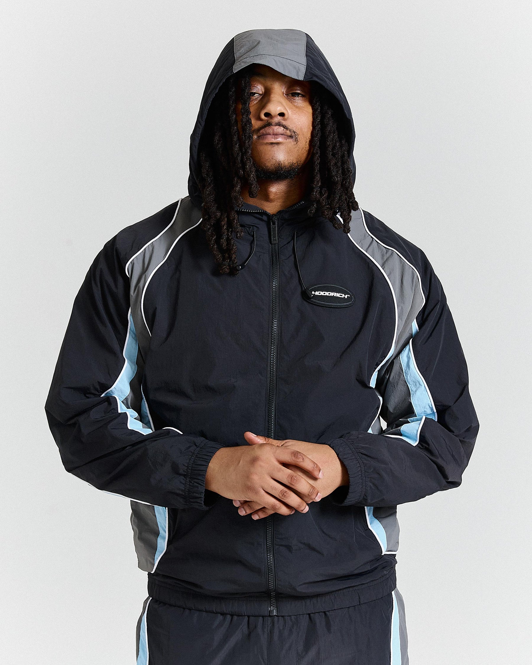 Person wearing a black and gray jacket with a hood on a light gray background