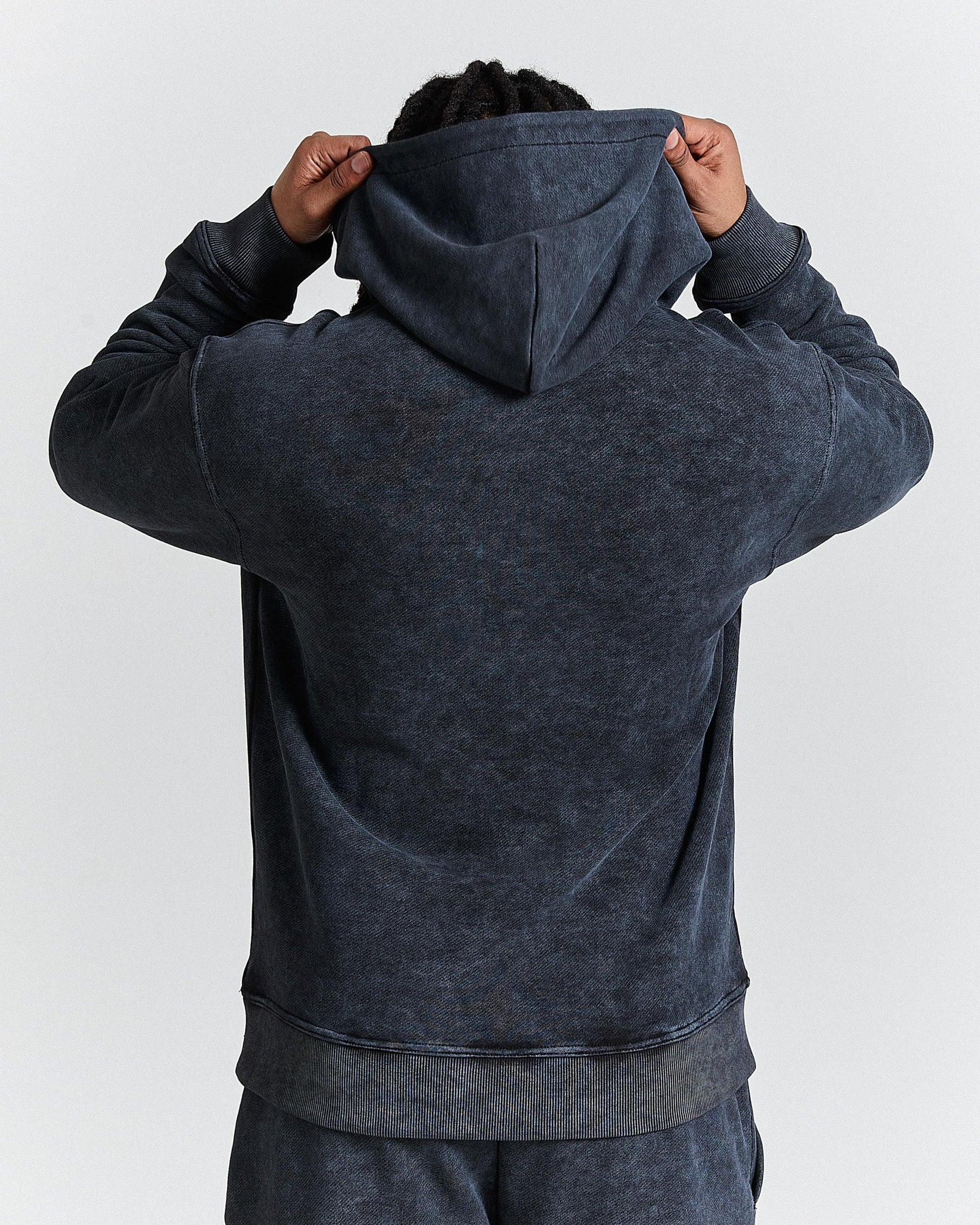 Person wearing a dark gray hoodie with the back facing the camera on a white background