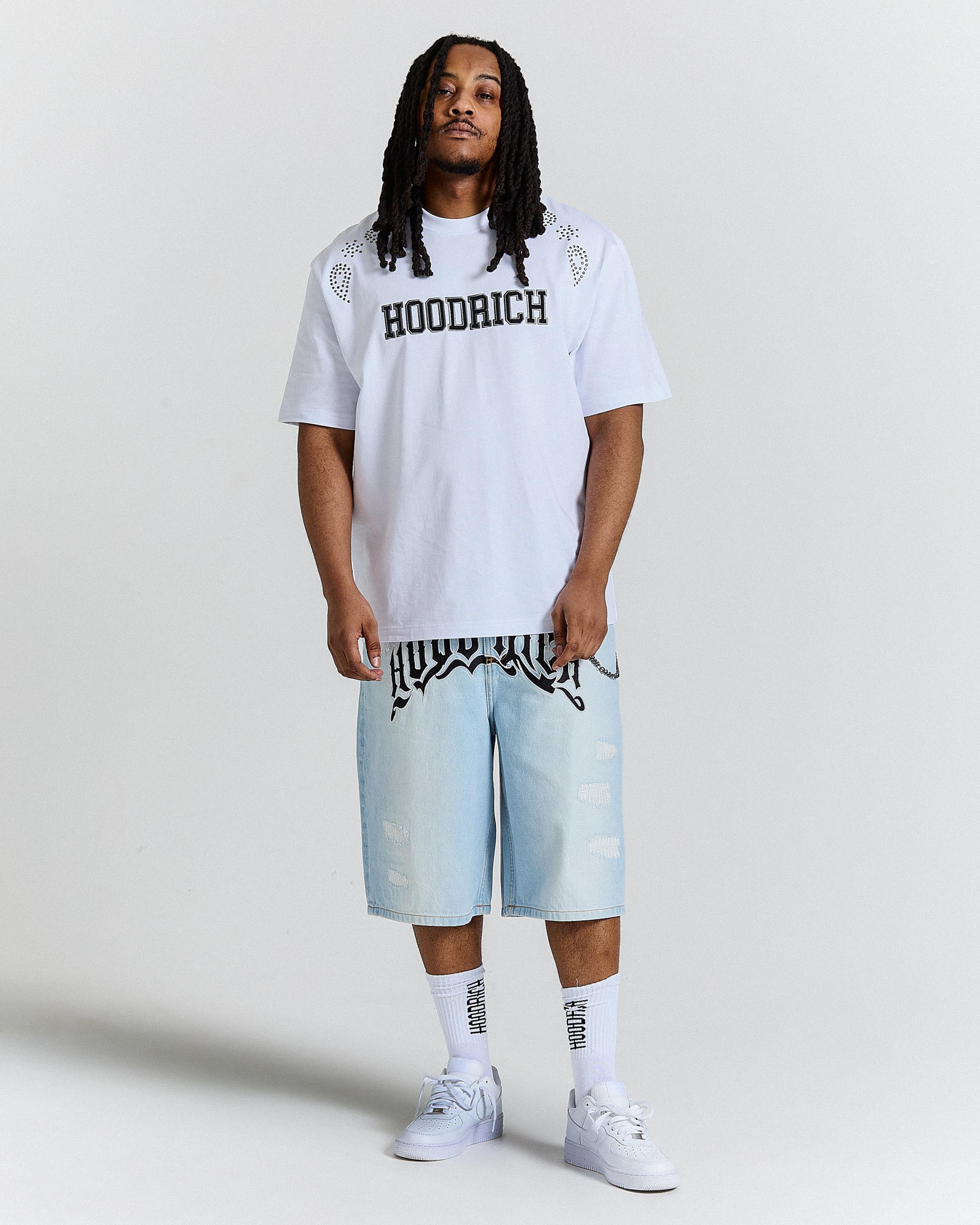 Person wearing a white 'Hoodrich' t-shirt and light blue shorts on a plain background