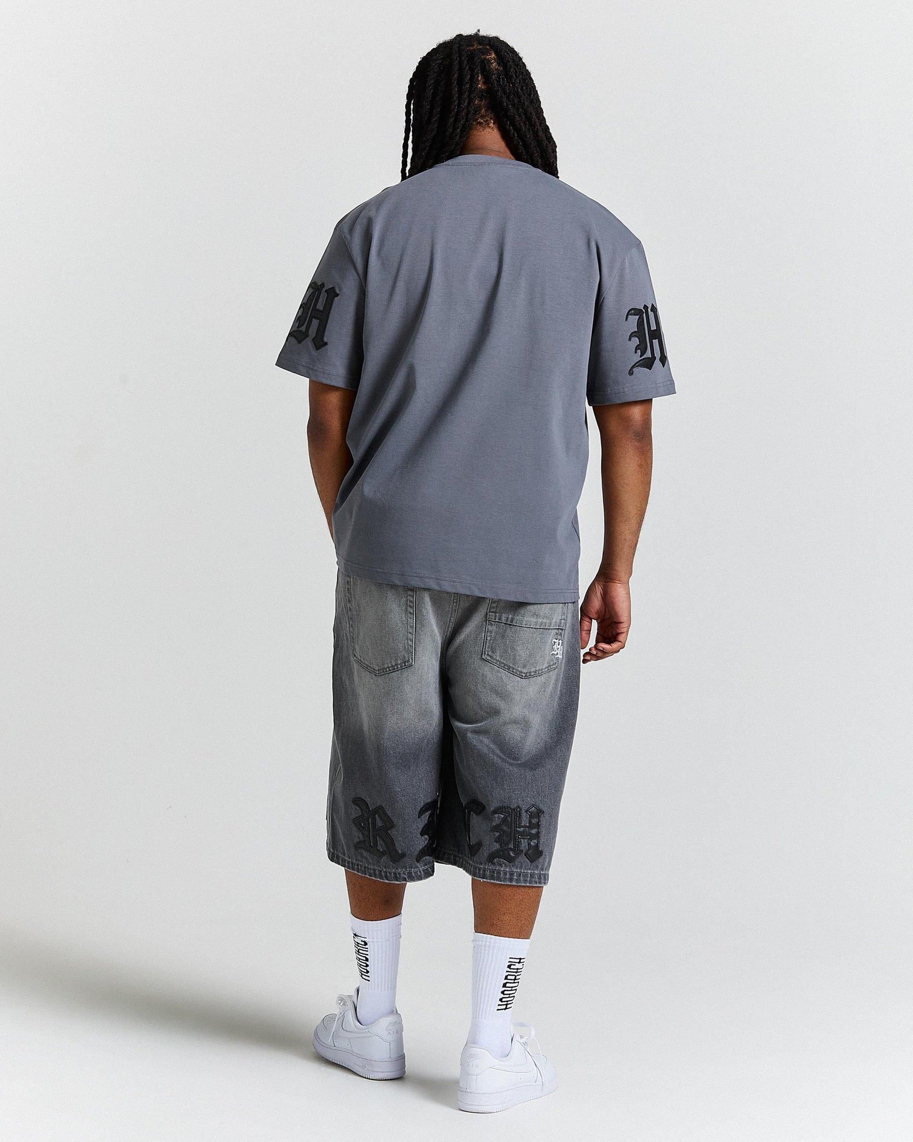 Person wearing a gray t-shirt and denim shorts with branding on a white background