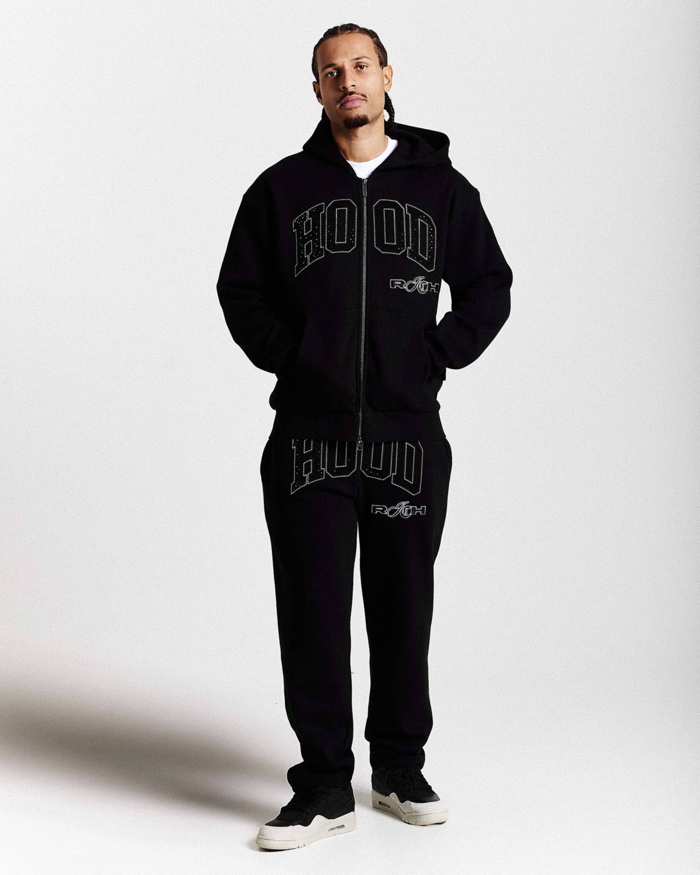 Person wearing a black 'HOODRICH' branded tracksuit on a white background