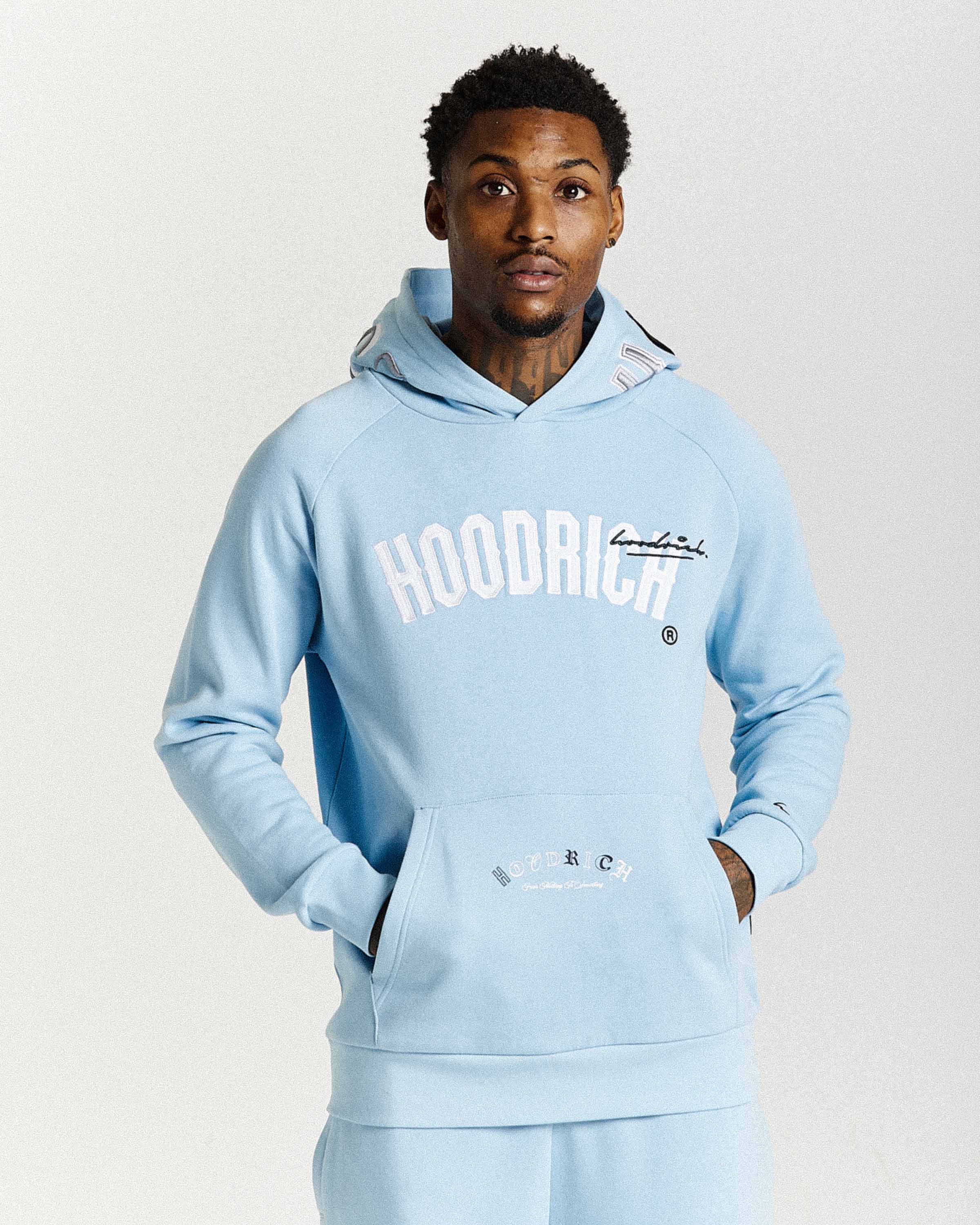 Man wearing a light blue 'HOODRICH' hoodie on a white background