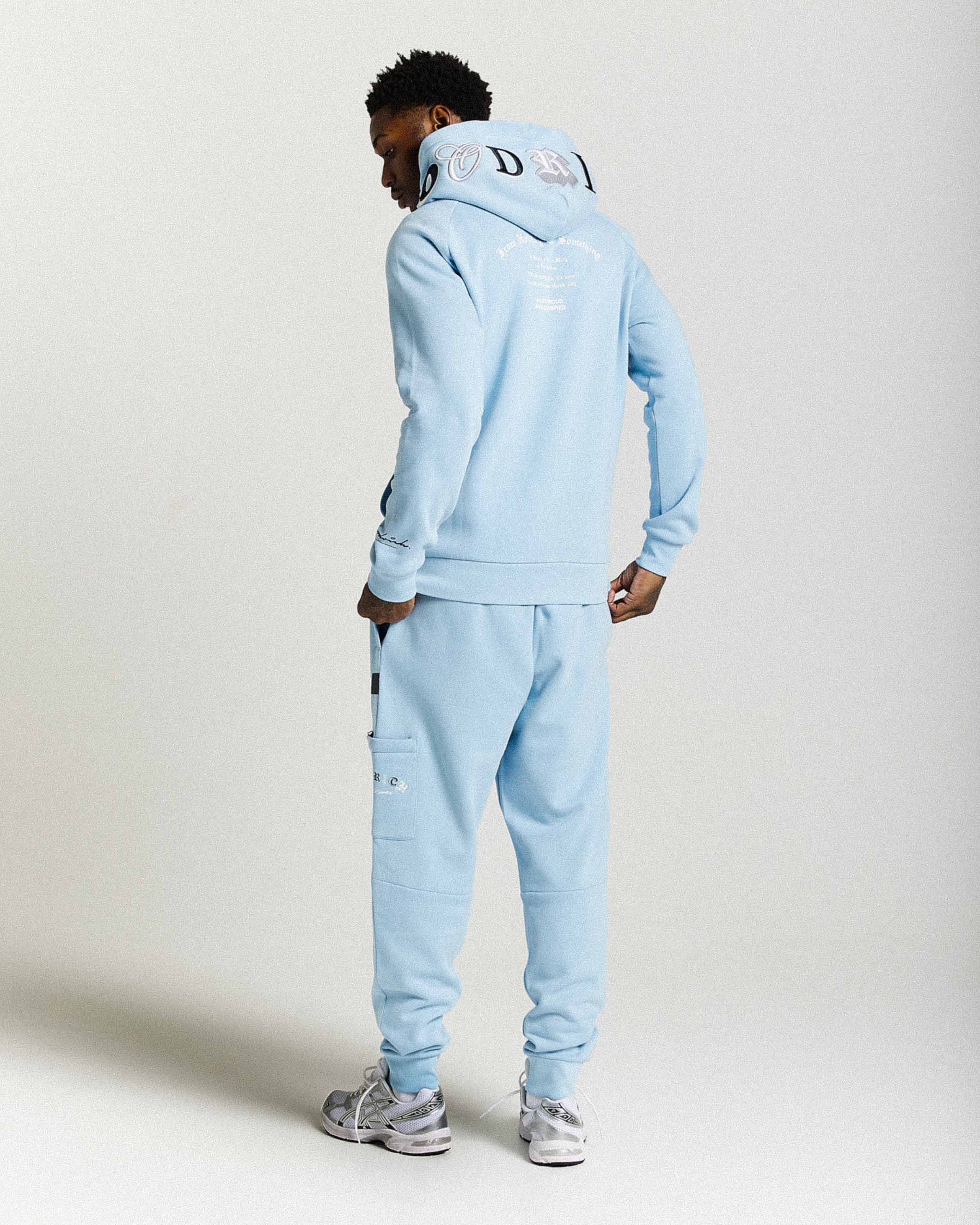 Person wearing a light blue tracksuit with brand logo on a white background