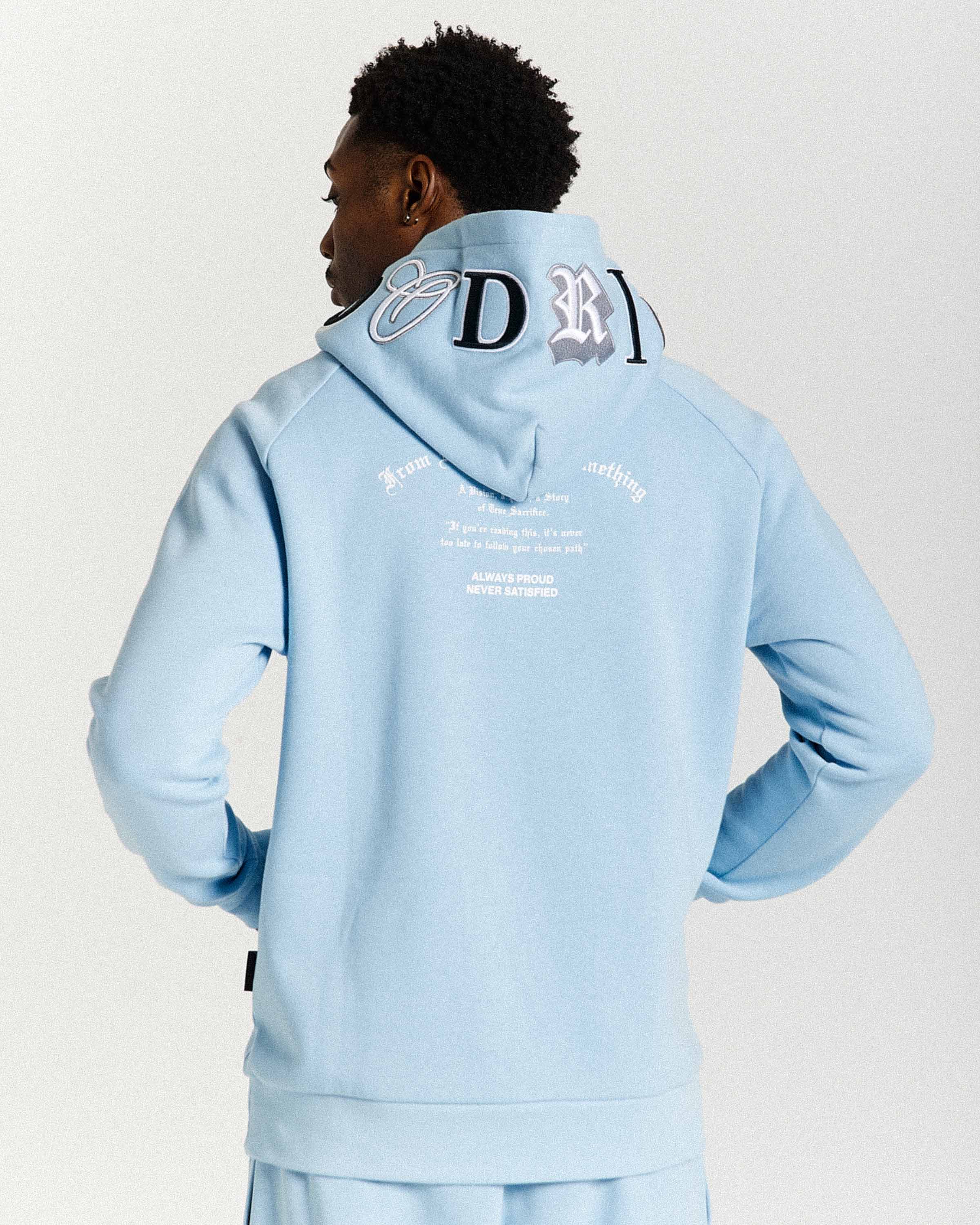 Person wearing a light blue hoodie with branding on the back against a white background