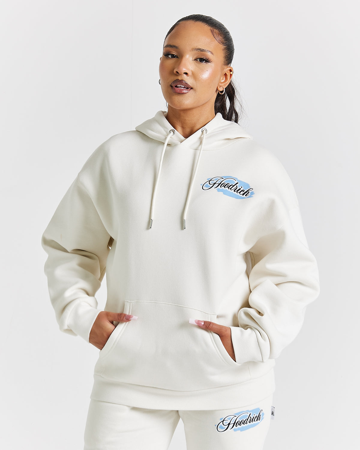 Displays a model wearing the White 'Hoodrich' branded women's Grillz Full Tracksuit 